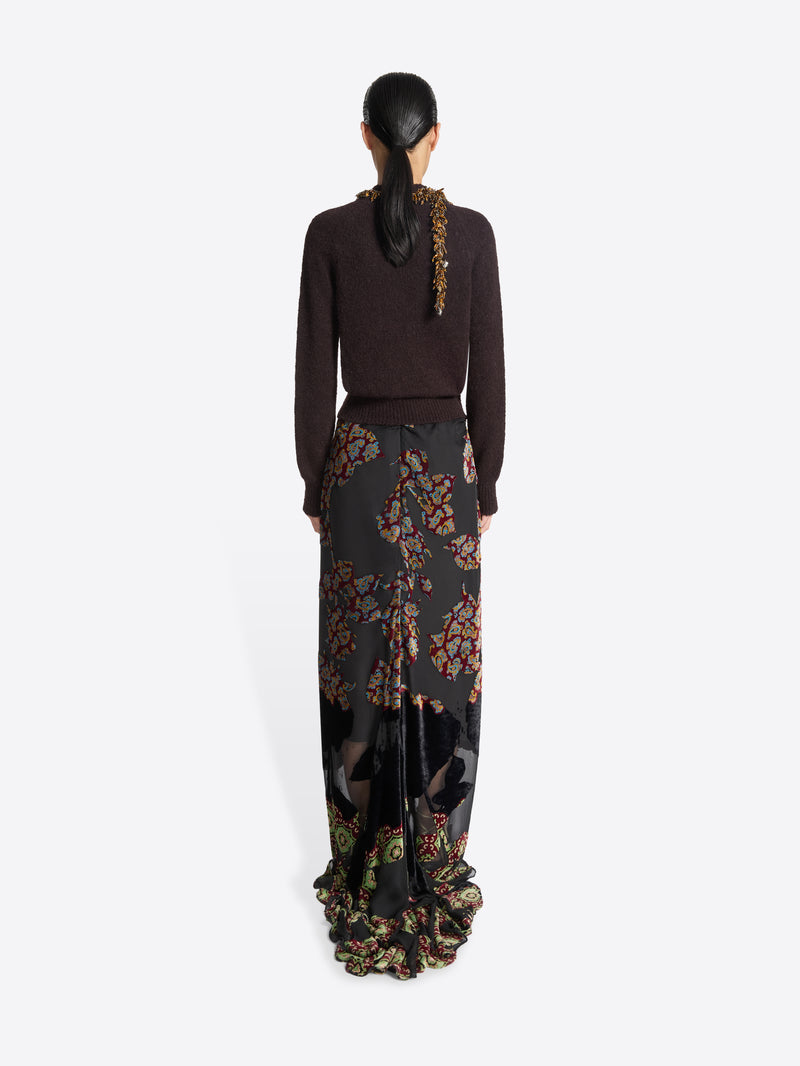 Model wearing a dark brown sweater and long, black, floral patterned skirt on a white background