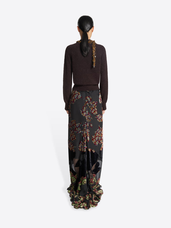 Model wearing a dark brown sweater and long, black, floral patterned skirt on a white background