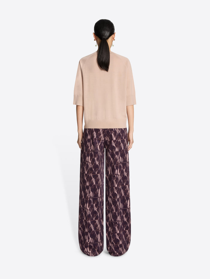 Woman wearing a light pink top and burgundy patterned pants on a white background