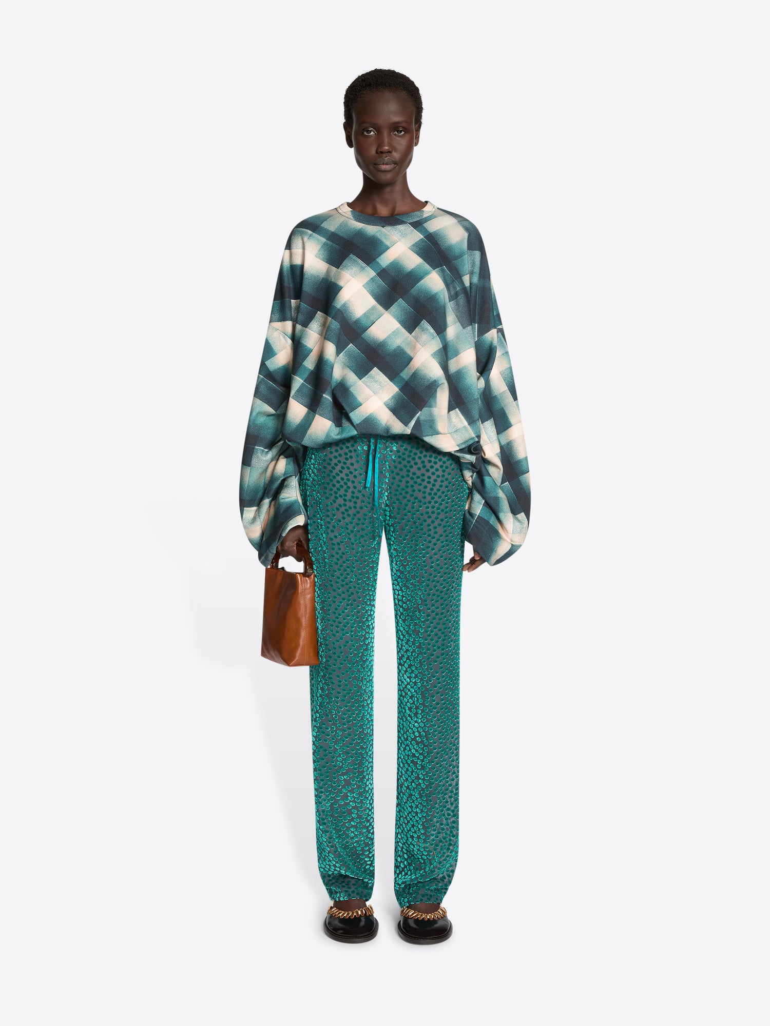 Person wearing a tie-dye sweater and teal pants on a white background