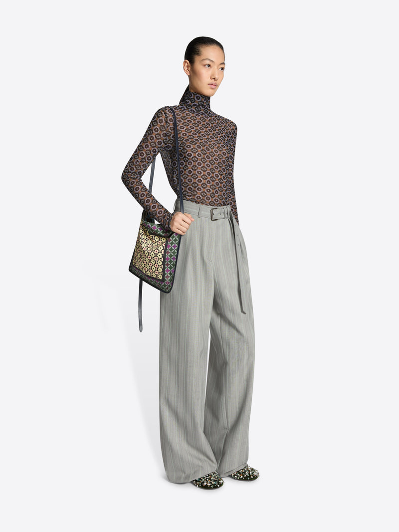 Model wearing a patterned top and gray pants with a handbag on a white background