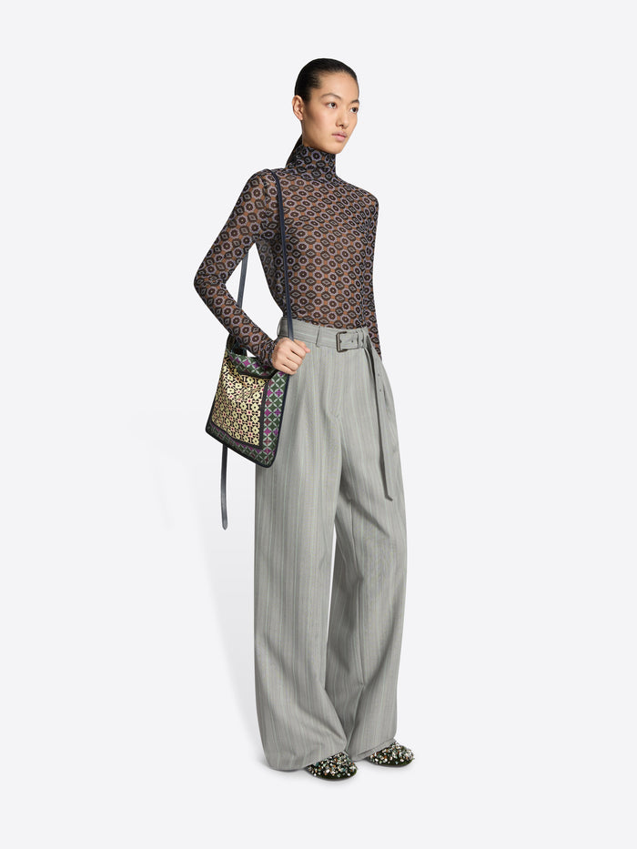Model wearing a patterned top and gray pants with a handbag on a white background