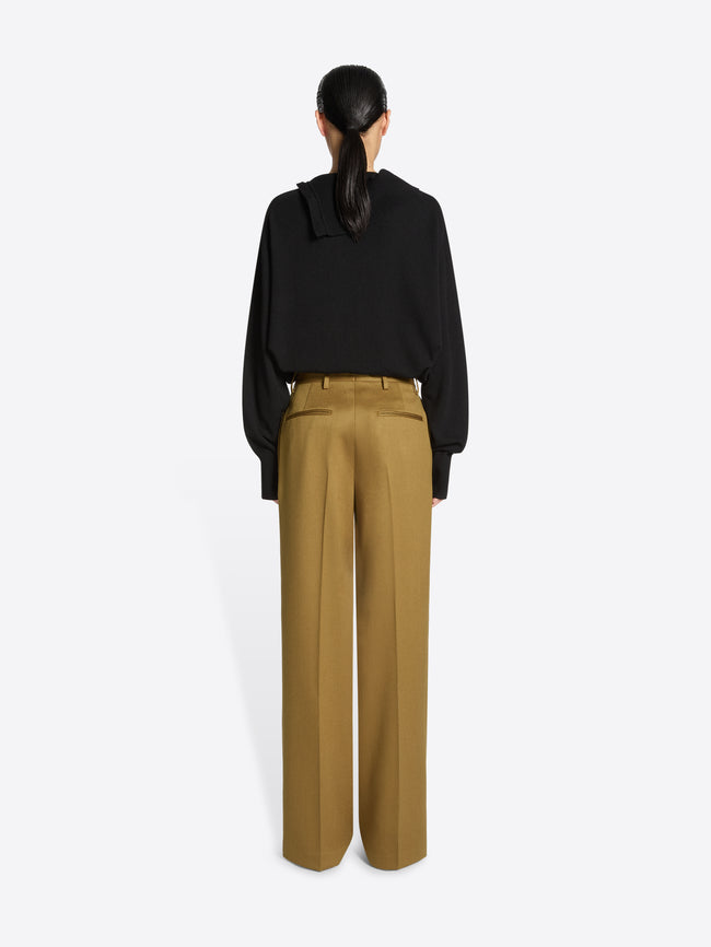 Backside of a person wearing a black top and umber colored pants on a white background