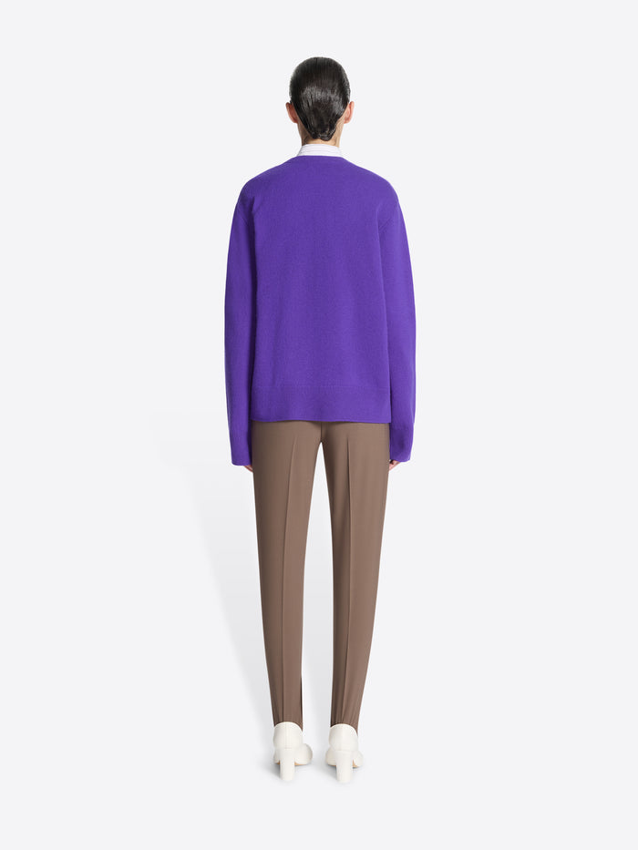 Backside of a person wearing a purple sweater, taupe stirrup pants, and white shoes on a white background.
