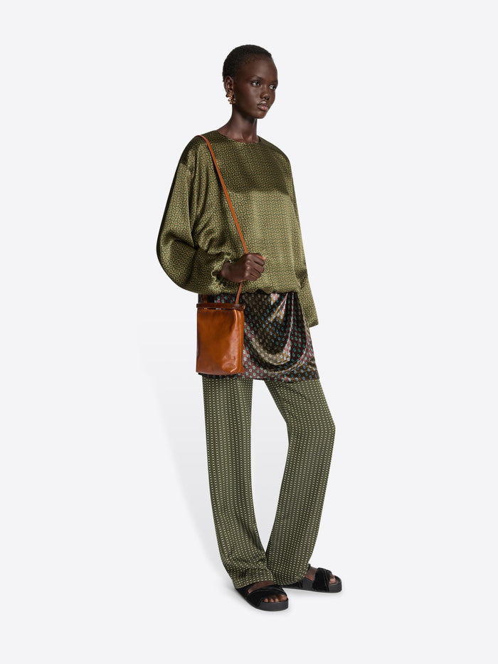Model wearing a green patterned outfit with a brown bag on a white background
