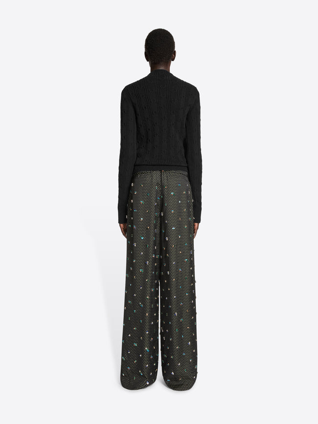 Backside of a person wearing a black sweater and a black embellished wide leg pants on a white background