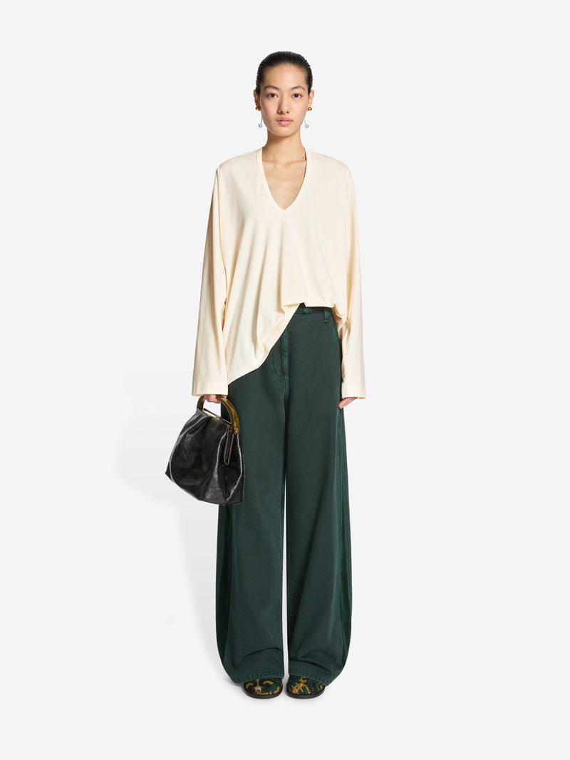 Woman wearing a cream top and green wide-leg pants with a black handbag on a white background