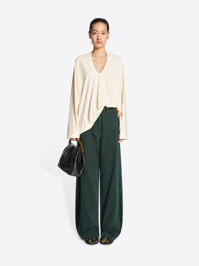 Woman wearing a cream top and green wide-leg pants with a black handbag on a white background