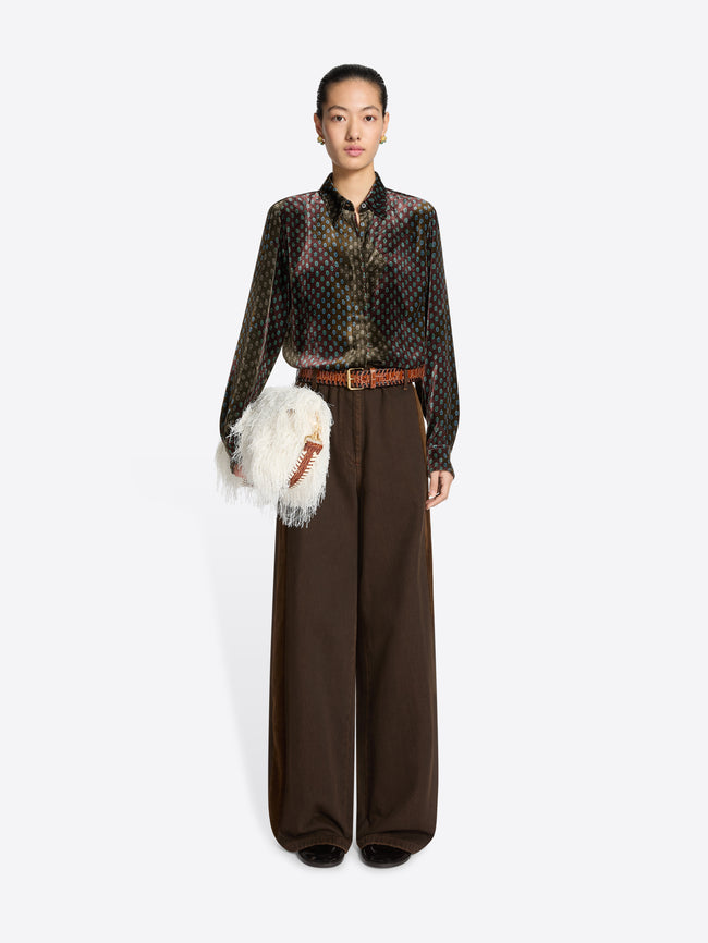 Person wearing a patterned shirt and brown pants holding a white fur bag on a white background