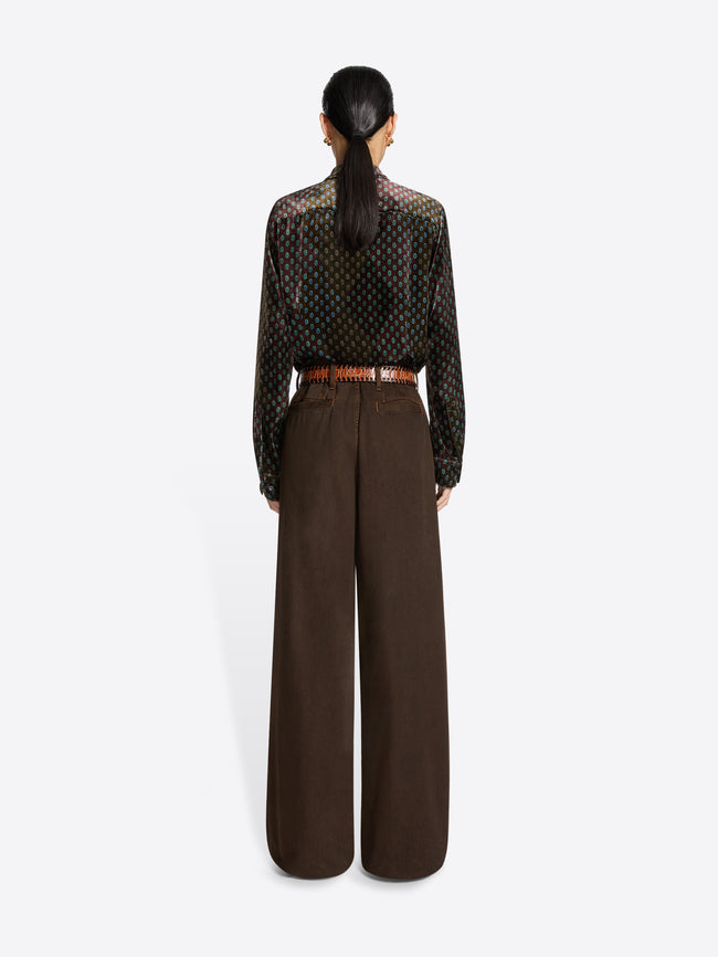 Person wearing a patterned shirt and brown wide-leg pants on a white background