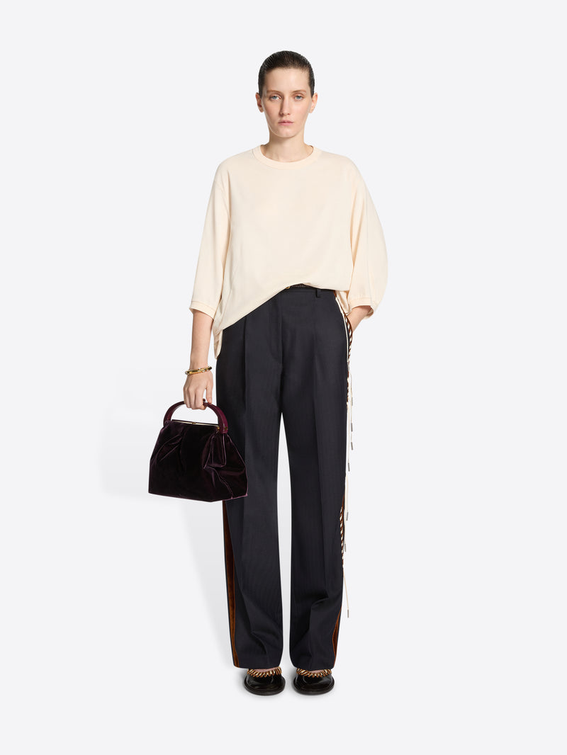 Person wearing a cream coloured sweater and navy pants with white and brown striped side tassels on a white background