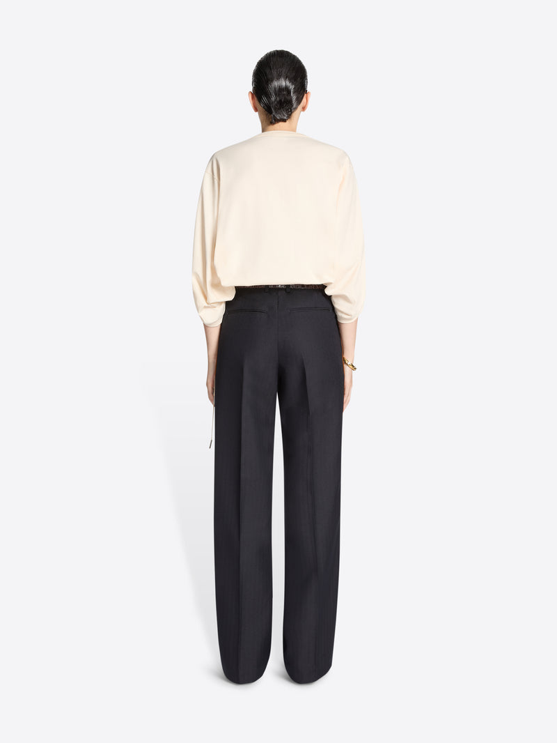 Person wearing a cream coloured sweater and navy pants with white and brown striped side tassels on a white background