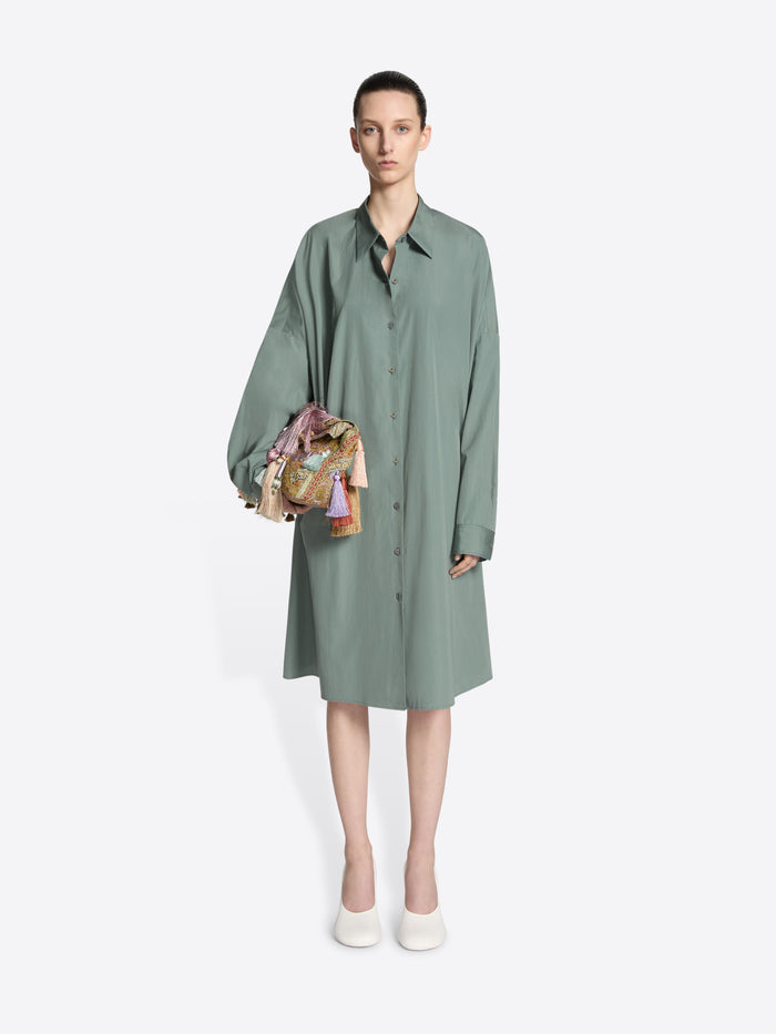 Model wearing a raf colored, oversized cotton shirt dress while wearing an embellished bag on a white background