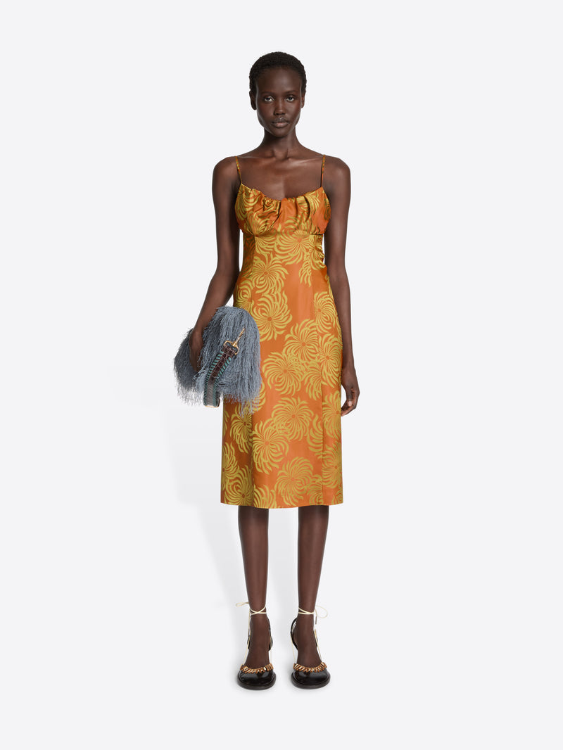 Woman wearing an orange dress with yellow floral pattern on a white background