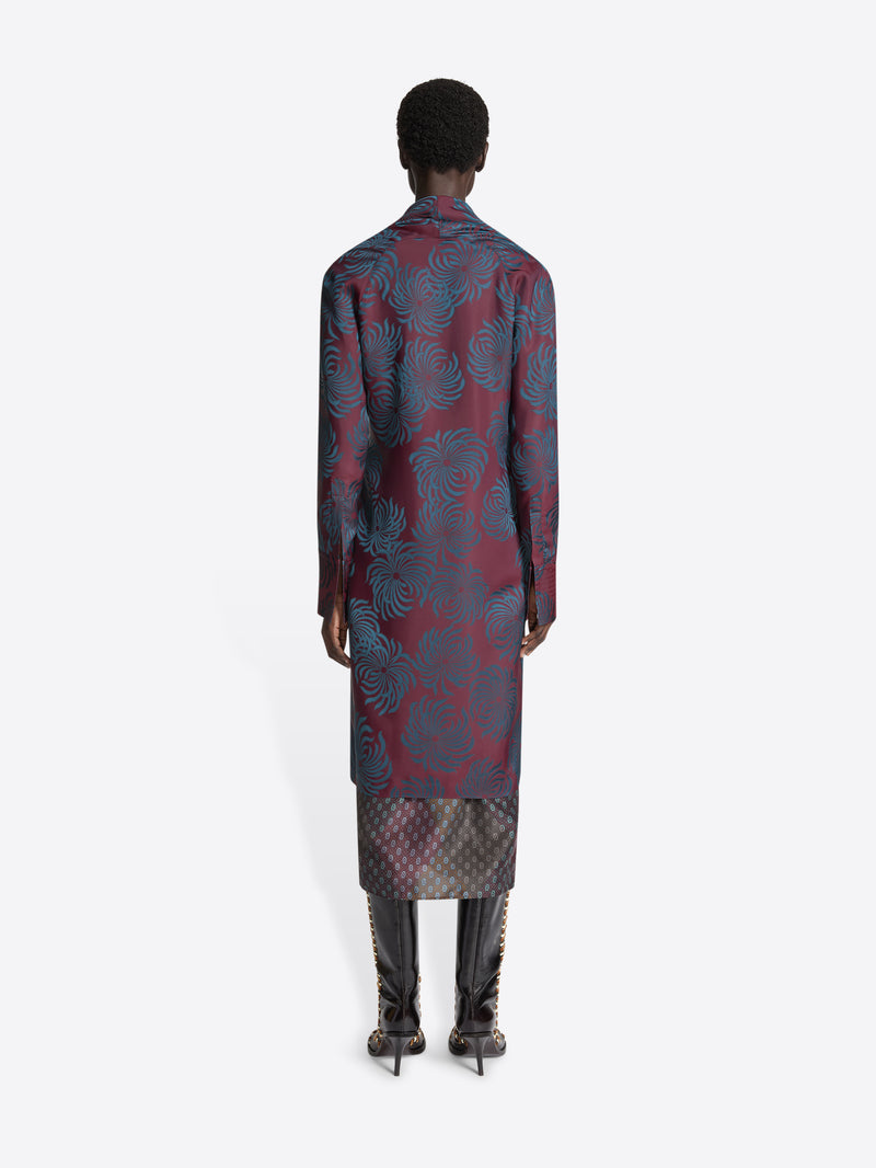 Person wearing a long burgundy patterned dress with a draped effect on a white background