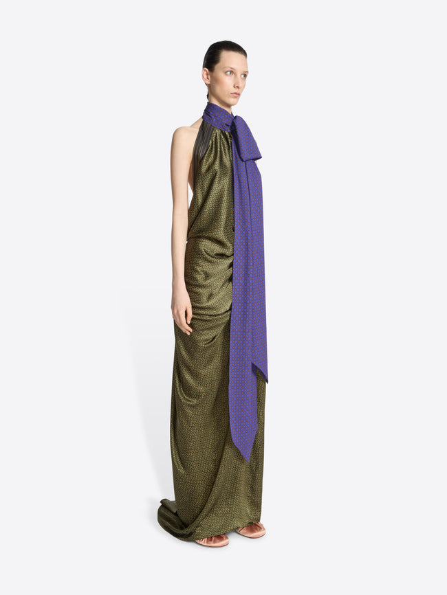 Model wearing a long green dress with a purple scarf on a white background