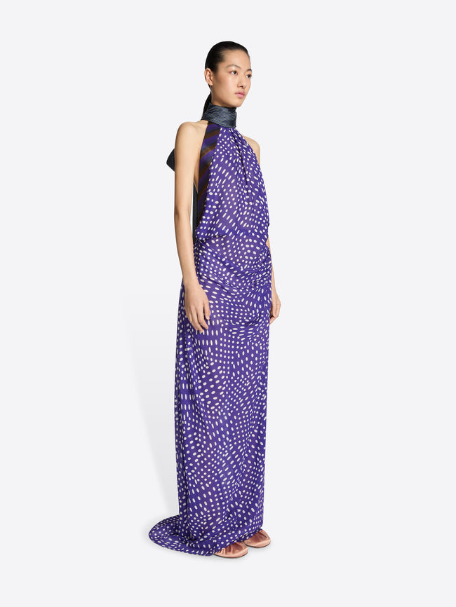 Woman wearing a long purple dress with white patterns on a white background