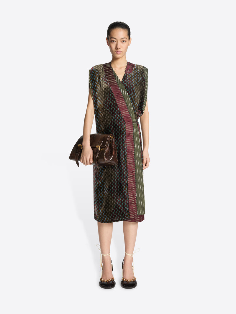 Woman wearing a patterned dress in khaki color mix holding a matching handbag on a white background