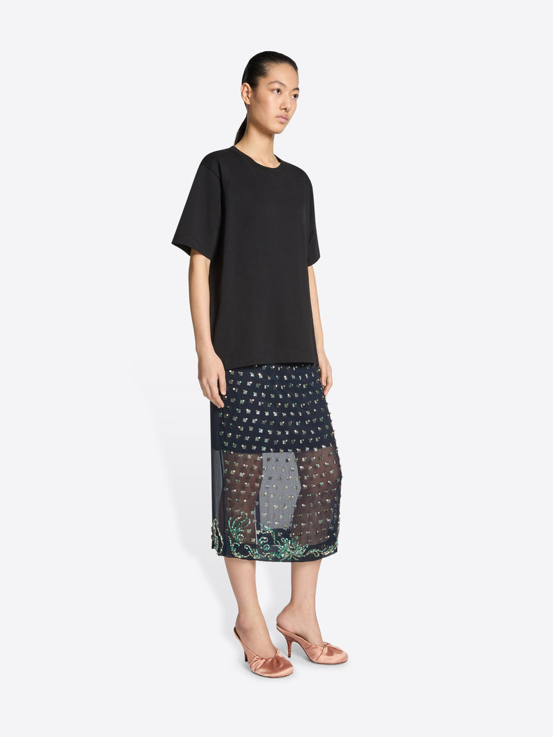 Woman wearing a black top and patterned skirt on a white background