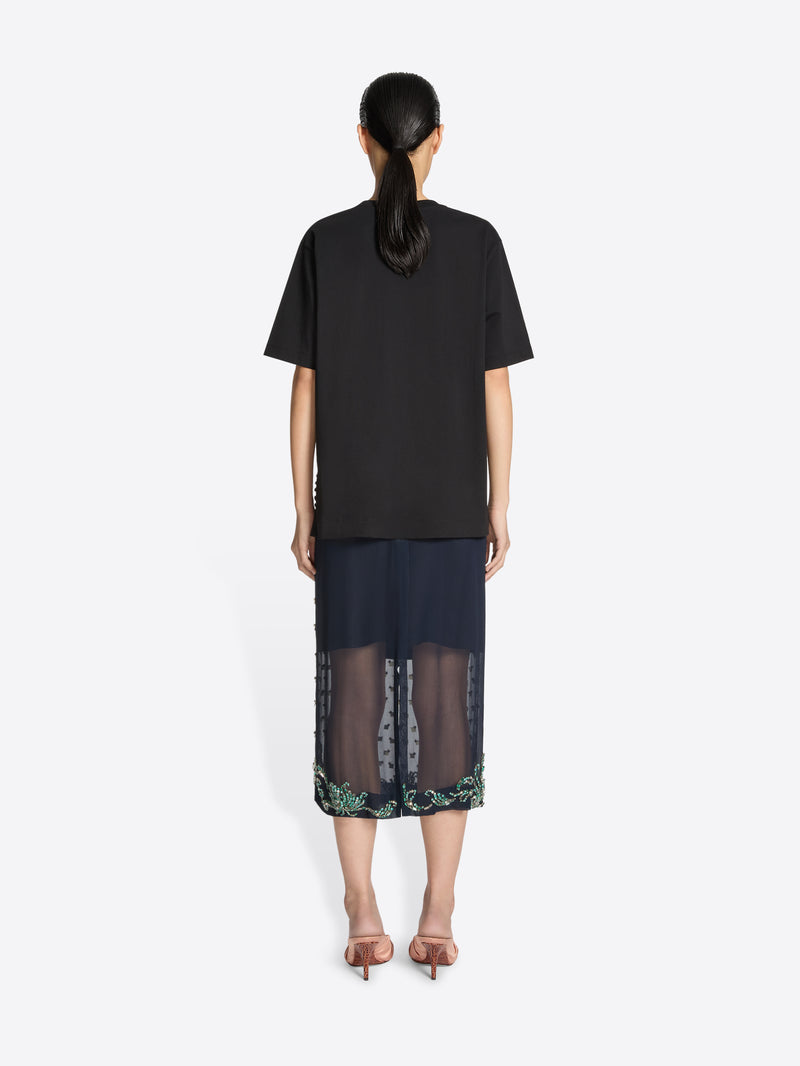 Person wearing a black top and dark skirt with floral pattern on a white background