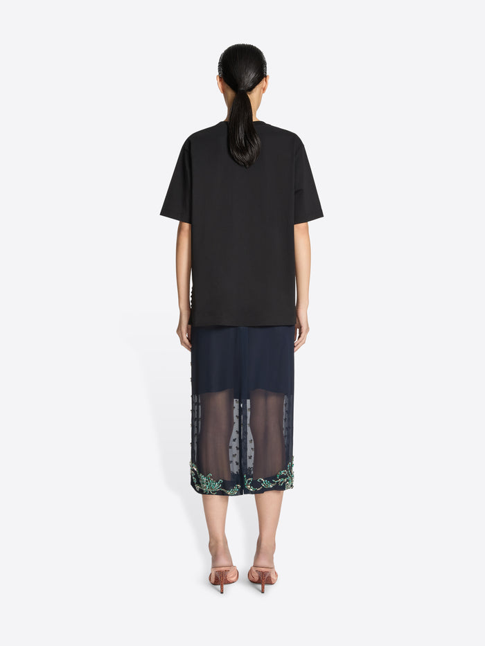 Person wearing a black top and dark skirt with floral pattern on a white background