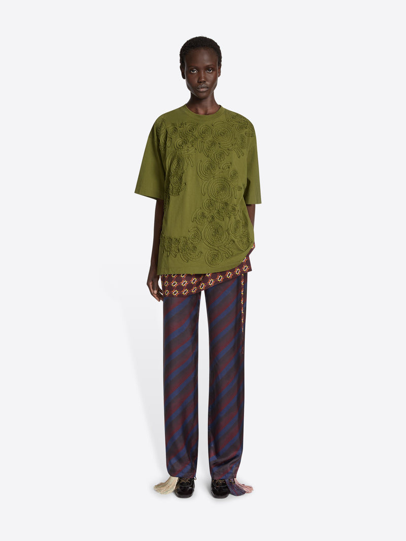 Model wearing a green embroidered cotton tee and navy skirt pants on a white background