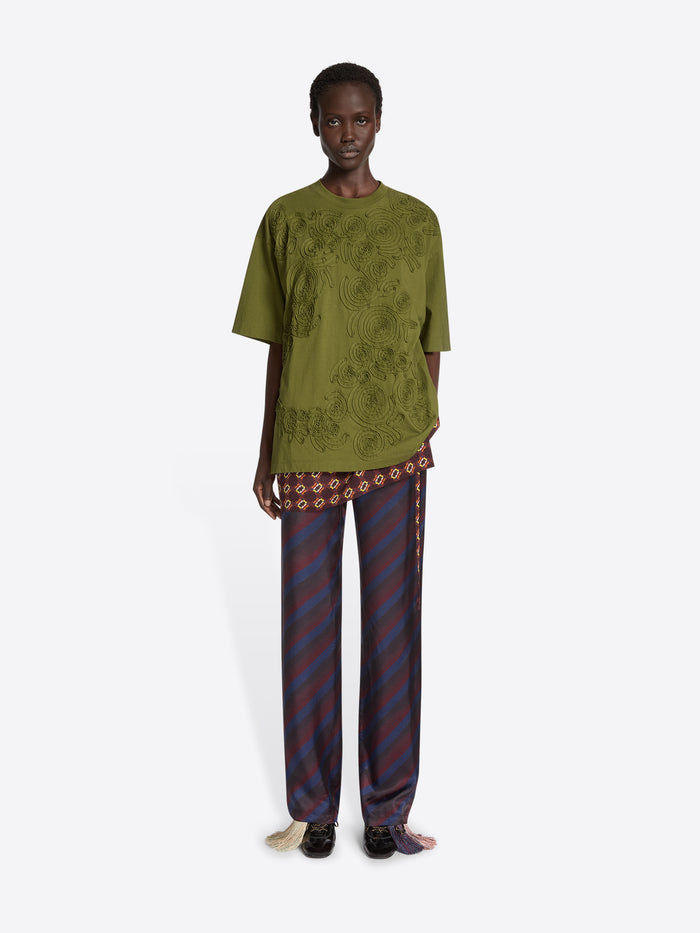 Model wearing a green embroidered cotton tee and navy skirt pants on a white background