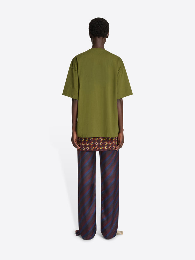 Backside of a model wearing a green embroidered cotton tee and navy skirt pants on a white background