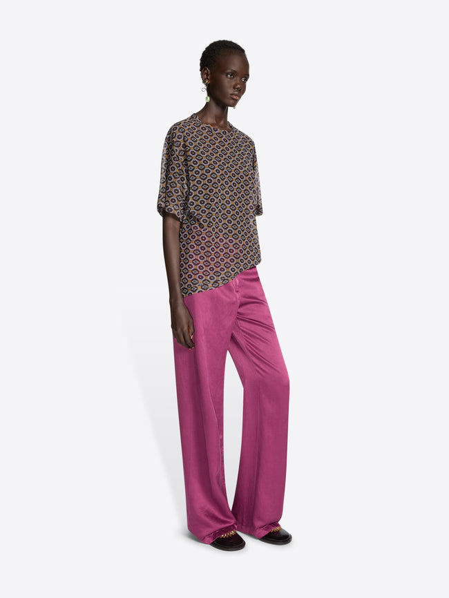 Model wearing a sheer oversized shirt with a brown patterned design and pink pants on a white background