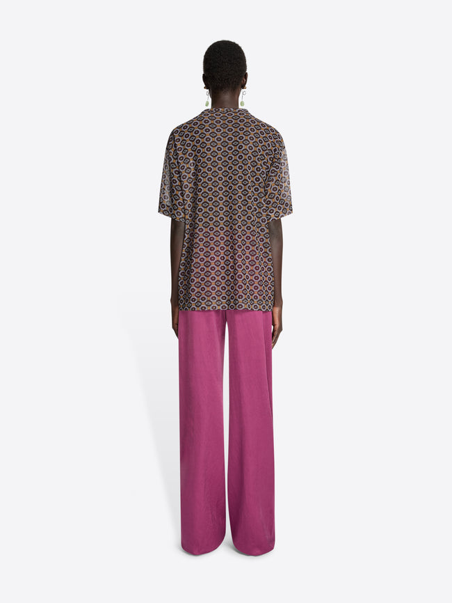 Backside of a model wearing a sheer oversized shirt with a brown patterned design and pink pants on a white background