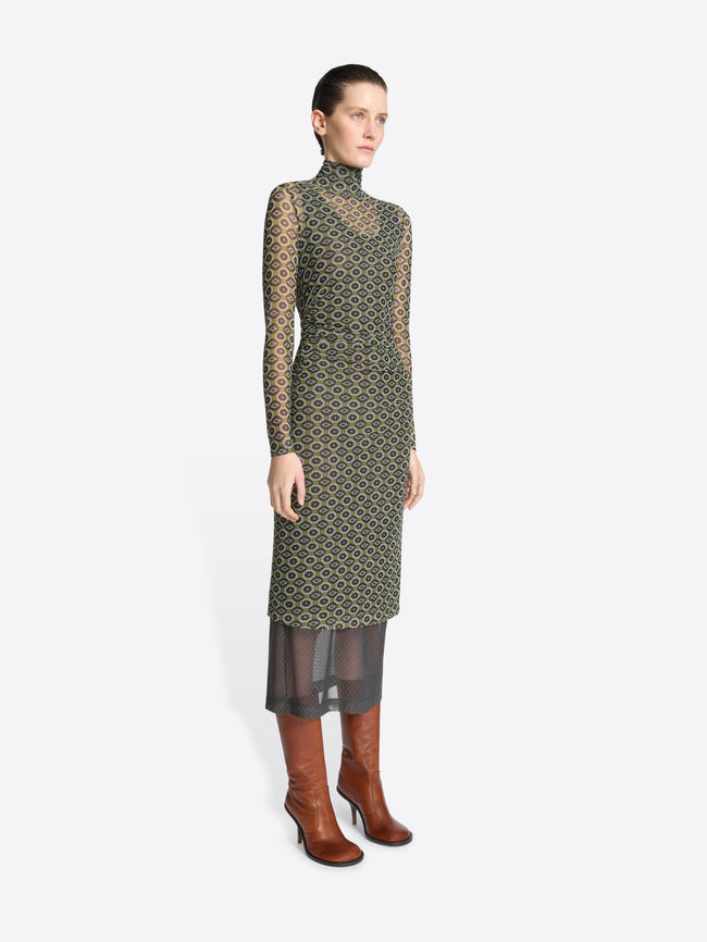 Woman wearing a green, long-sleeve printed mesh dress with geometric pattern on a white background