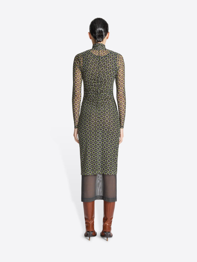 Backside of a woman wearing a green, long-sleeve printed mesh dress with geometric pattern on a white background