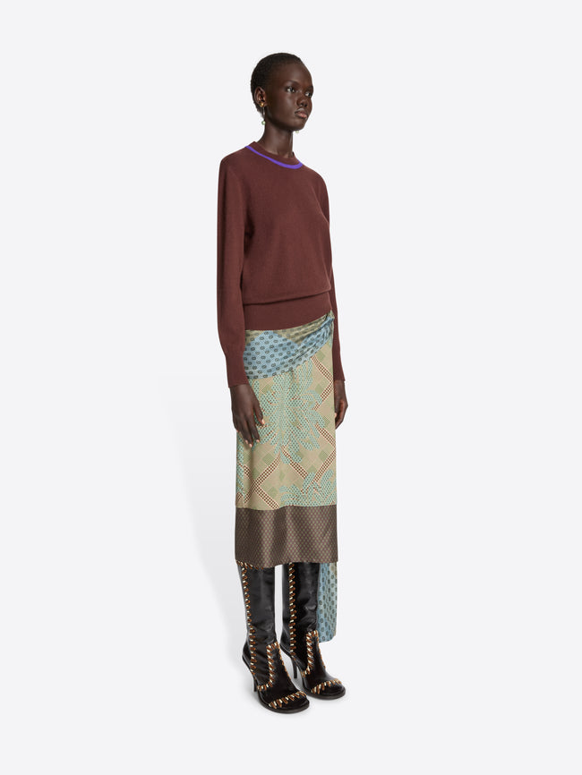 Model wearing a brown sweater and patterned skirt on a white background