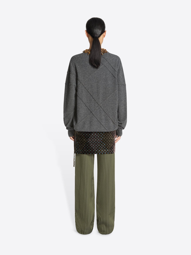 Backside of a model wearing a gray cashmere sweater with patterned accents and green skirt pants on a white background