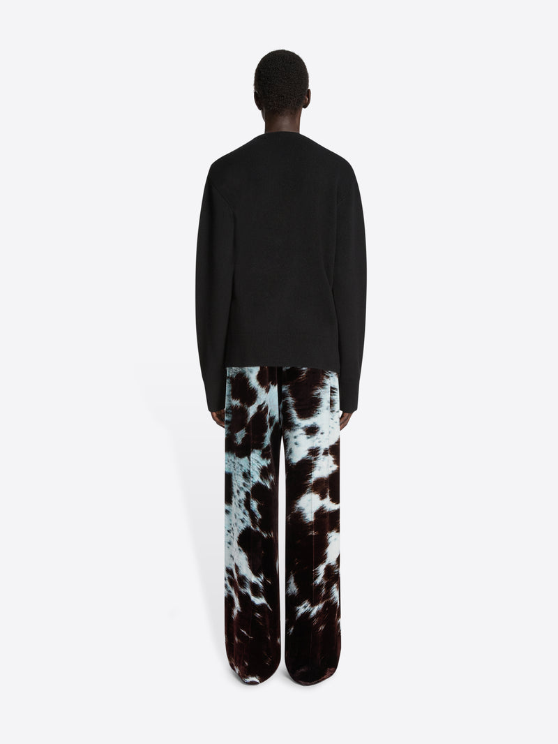 Backside of a model wearing a black, wrap-style cashmere sweater with embellished detail and cowhide patterned pants on a white background