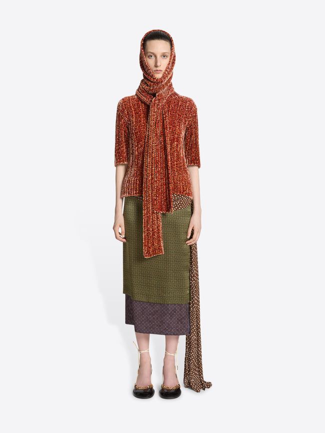 Model wearing a peach colored hooded scarf with a matching top and green skirt on a white background