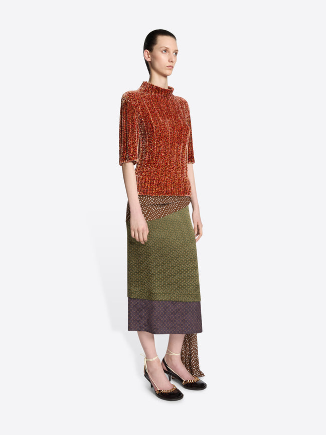 Model wearing a peach colored short sleeved sweater and a green skirt on a white background