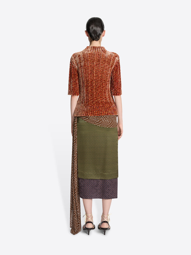 Backside of a model wearing a peach colored short sleeved sweater and a green skirt on a white background