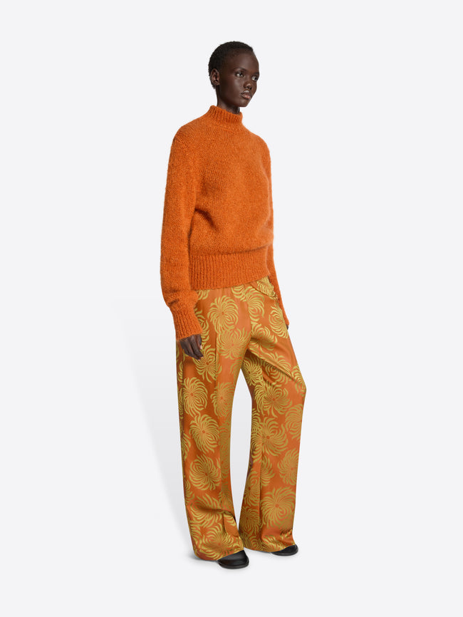 Person wearing an orange knit sweater and patterned pants on a white background