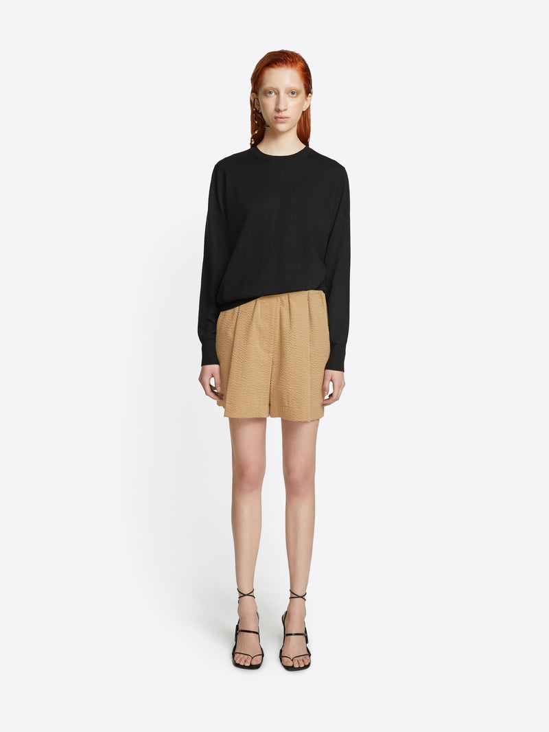 Woman wearing a black sweater and beige shorts on a white background