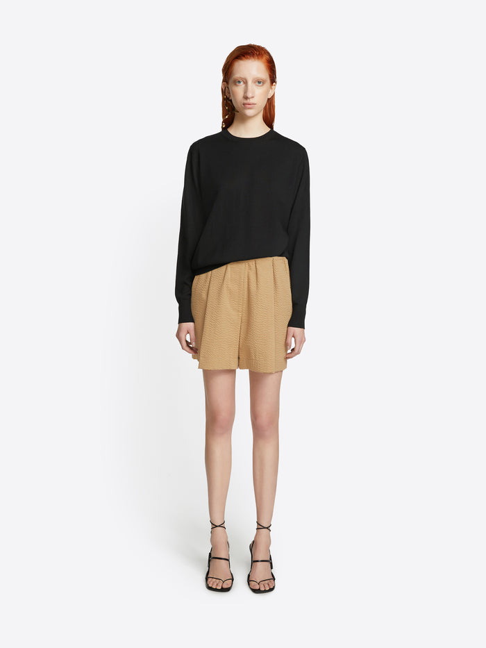 Woman wearing a black sweater and beige shorts on a white background