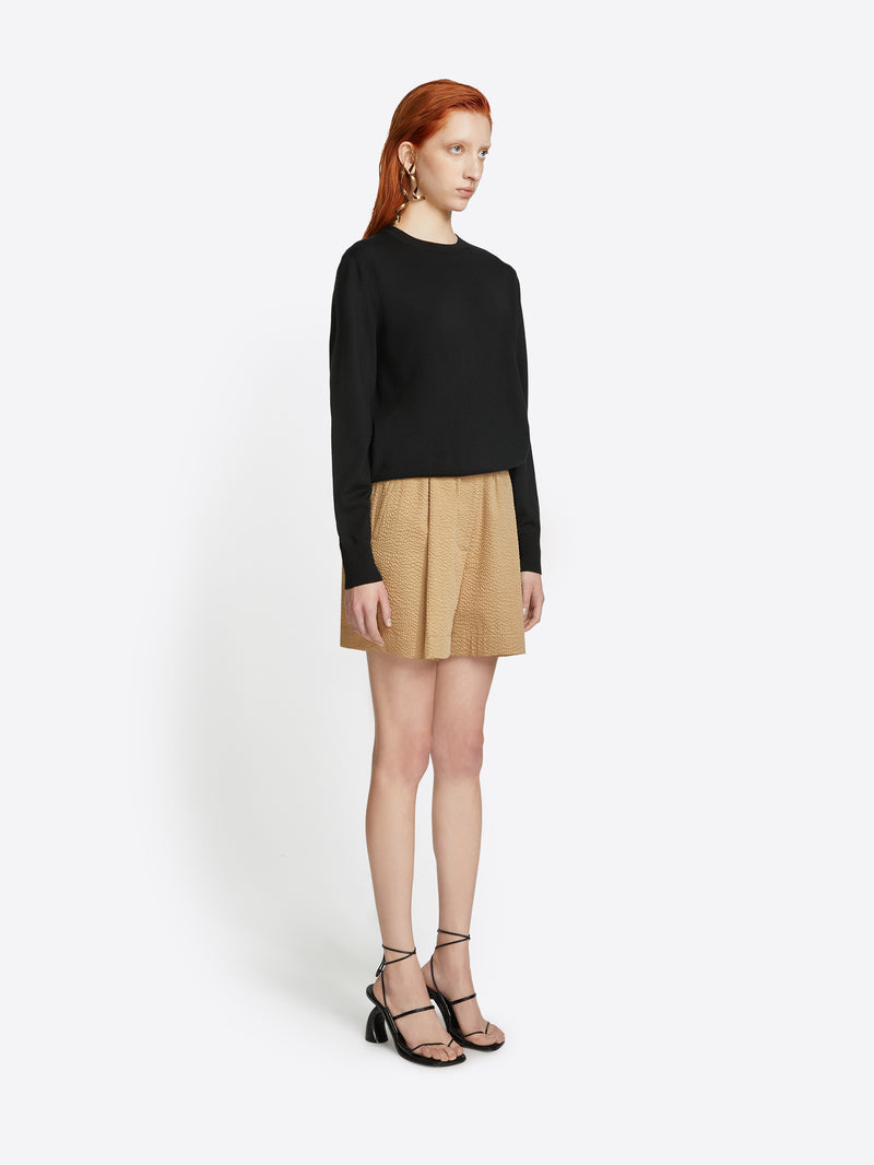 Woman wearing a black sweater and beige skirt on a white background