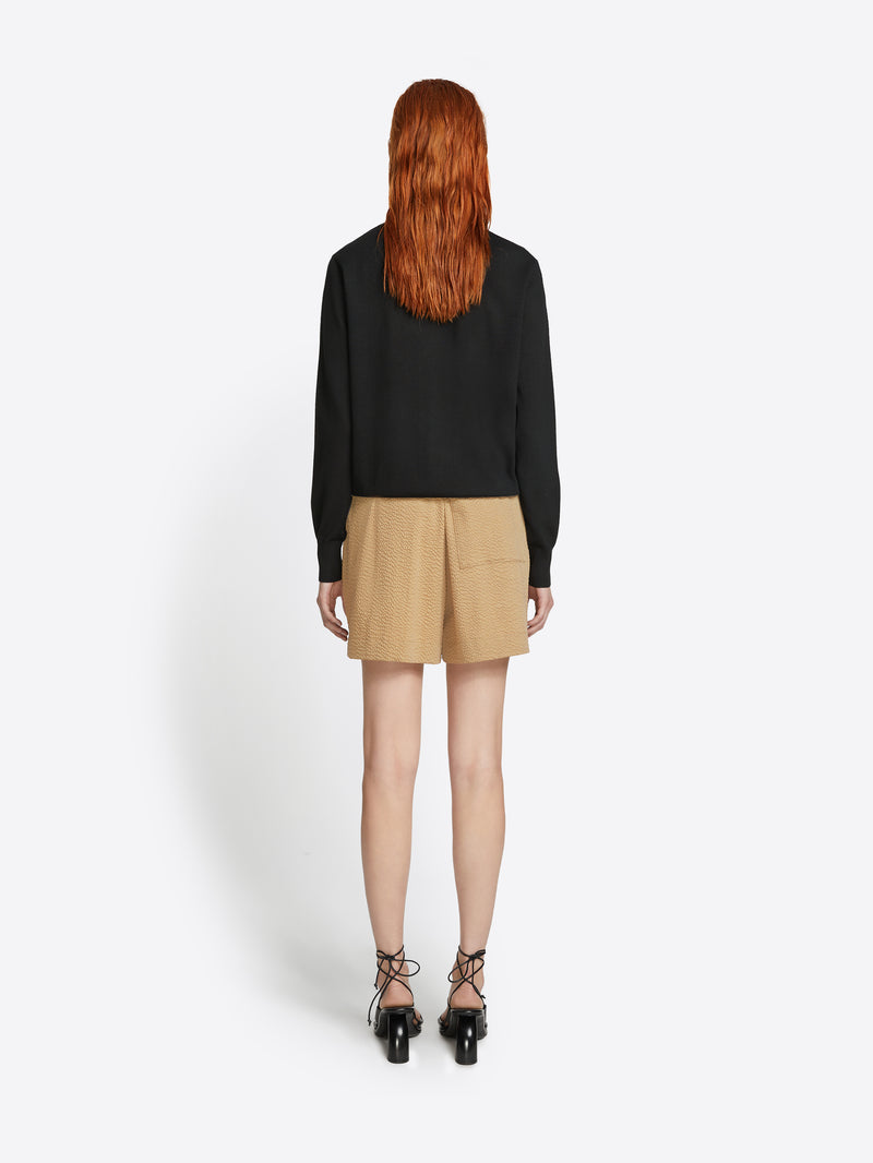 Person wearing a black top and beige skirt on a white background