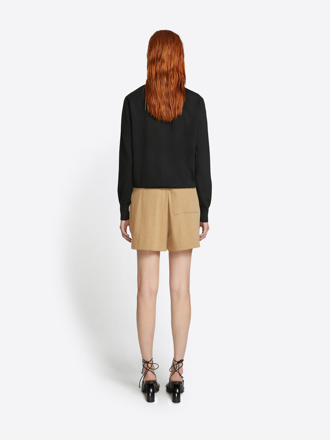 Person wearing a black top and beige skirt on a white background