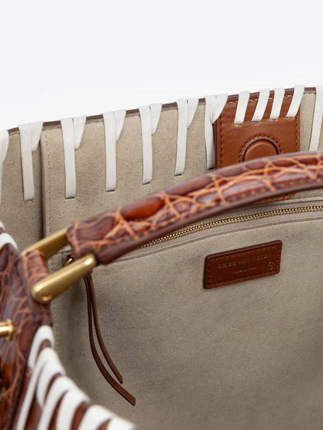 Close-up of a beige handbag with brown leather handle and gold zipper, featuring a brand logo.