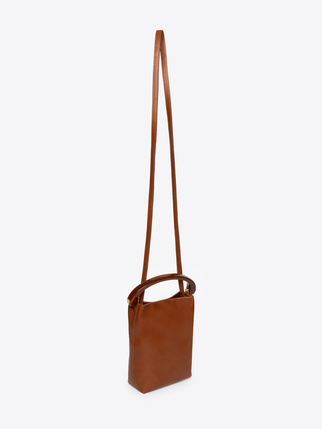 Brown micro leather handbag with a brown resin handle and a long strap on a white background