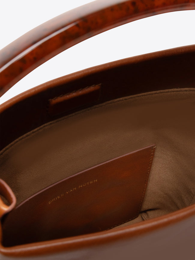 Close-up of a tan leather handbag with Dries Van Noten label on a white background