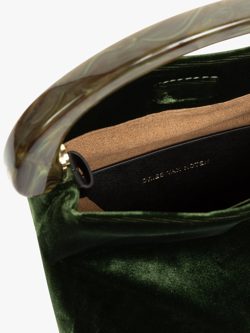 Close-up of a green handbag with a gold handle and visible brand name.