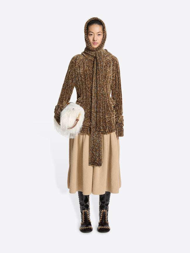 Person wearing a brown knitted hooded coat with a beige skirt on a white background