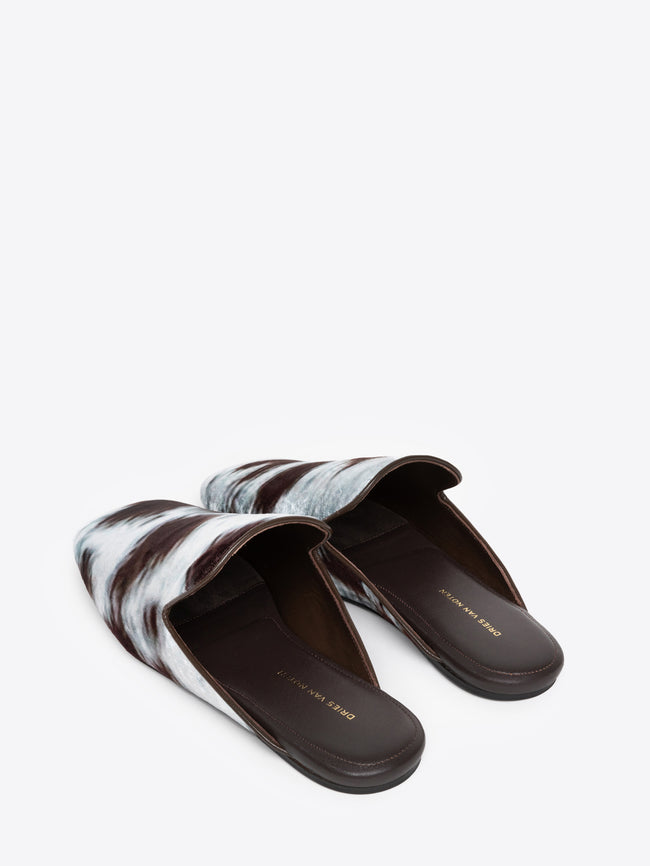 Backside of a pair of cowhide motif printed mules on a white background